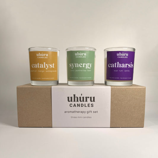 Uhuru Candle aromatherapy gift set. Three mini candles with labels 'catalyst', 'synergy', and 'catharsis' from Uhuru Candles on a beige box.
