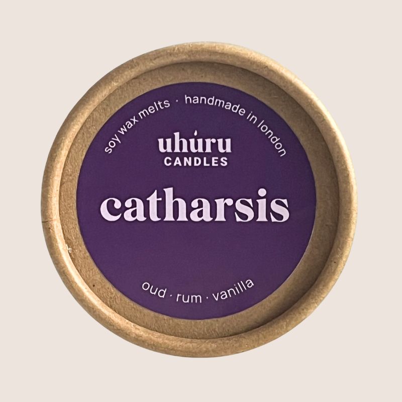 Soy wax melts container with purple lid labeled 'Catharsis' by Uhuru Candles on a beige background