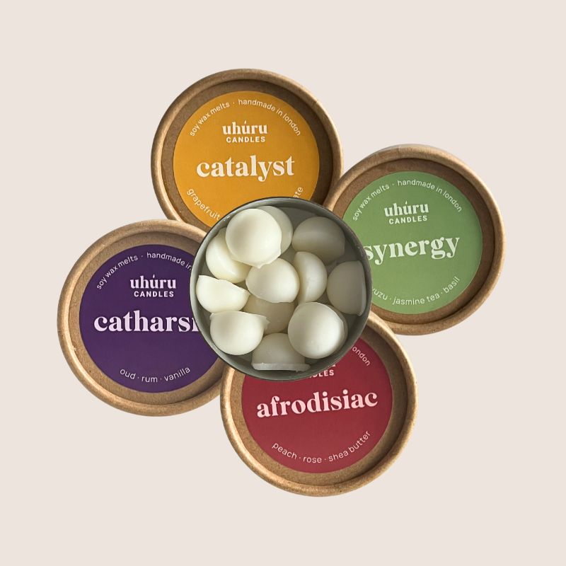 Five small containers labeled 'catharsis', 'catalyst', 'synergy', 'afrodisiac' with a central container showing white wax melts.