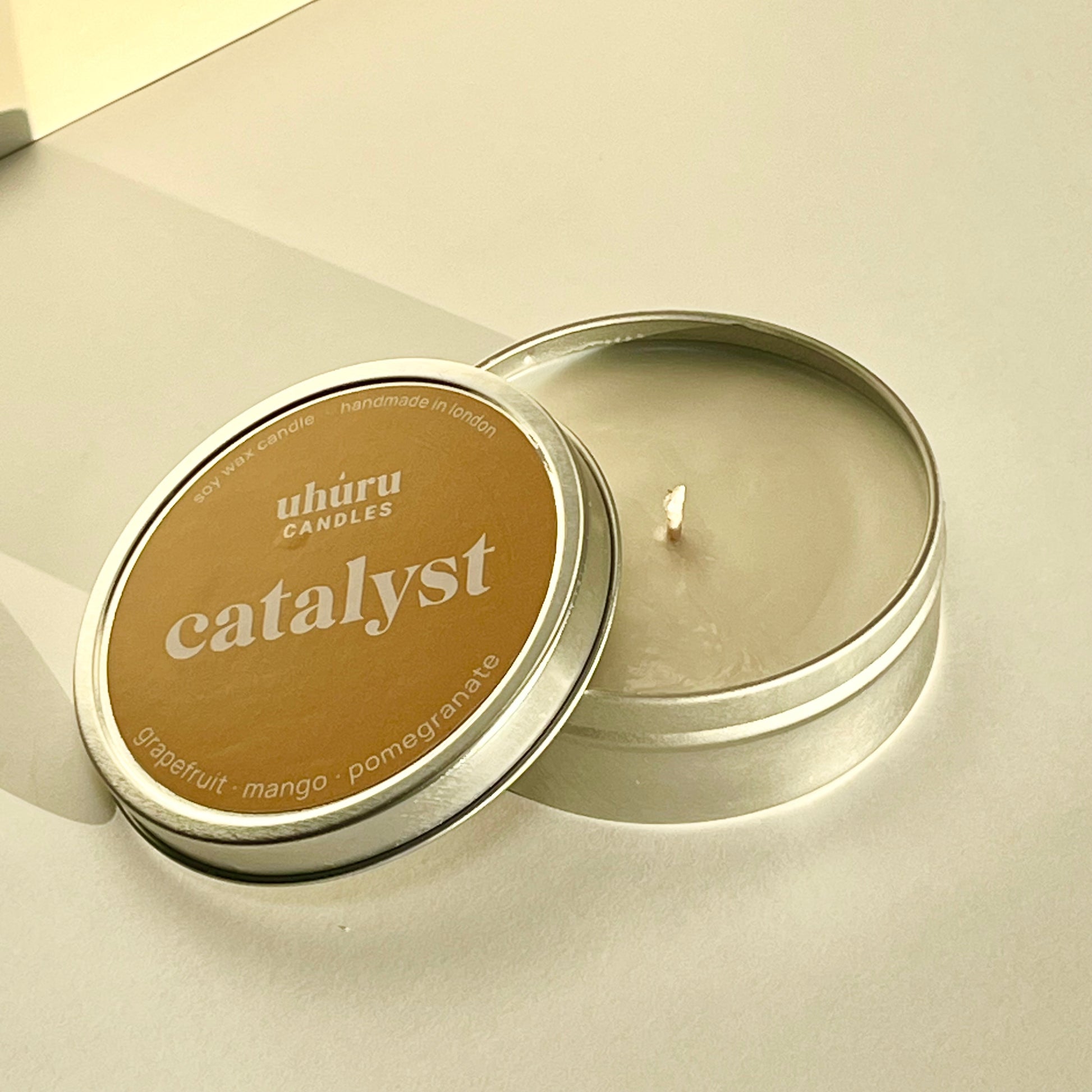 Catalyst by Uhuru Candles - grapefruit, mango and pomegranate scented soy wax candle in tin container with lid off. Net weight 70g.