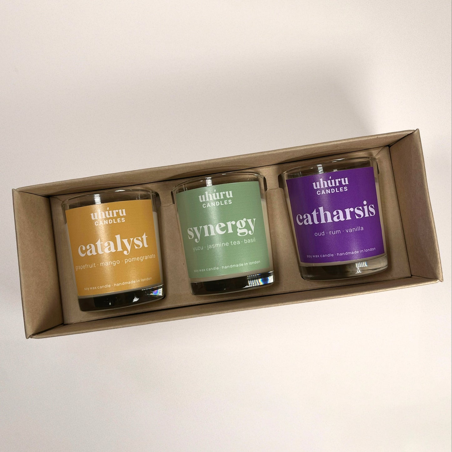 Uhuru Candles aromatherapy gift set. Three candles in a box labeled 'catalyst', 'synergy', and 'catharsis' on a light background.