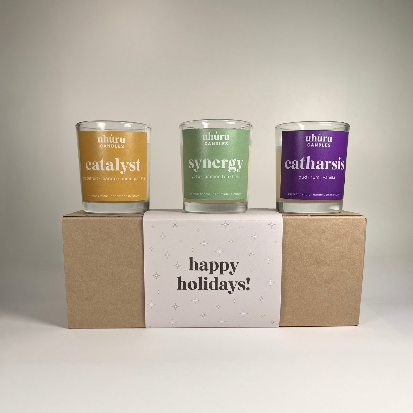 Uhuru Candles aromatherapy gift set. Three candles in different colors on a box with 'happy holidays!' text, against a neutral background.