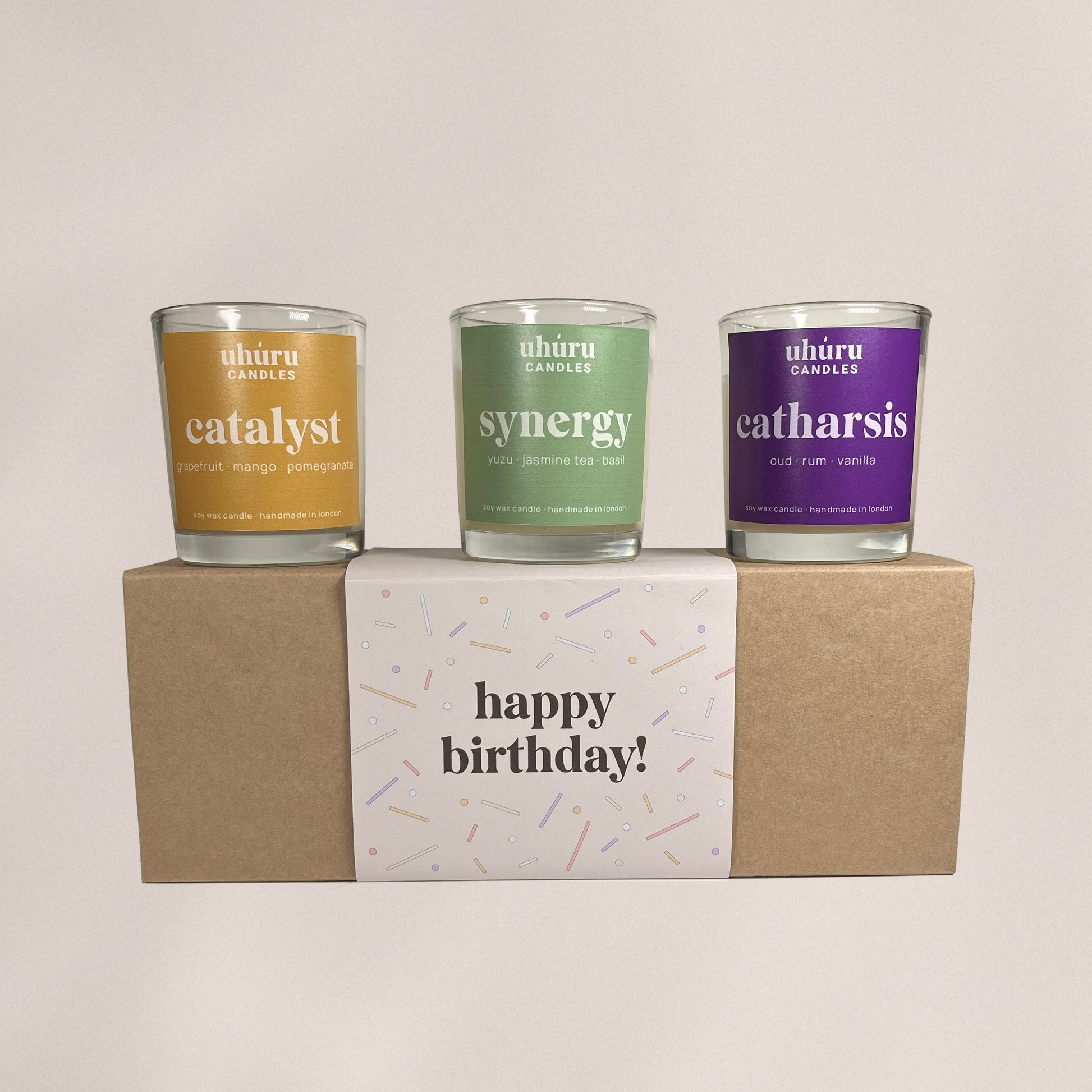 Uhuru Candles aromatherapy gift set. Three candles labeled 'catalyst', 'synergy', and 'catharsis' on a box with 'happy birthday!' text.