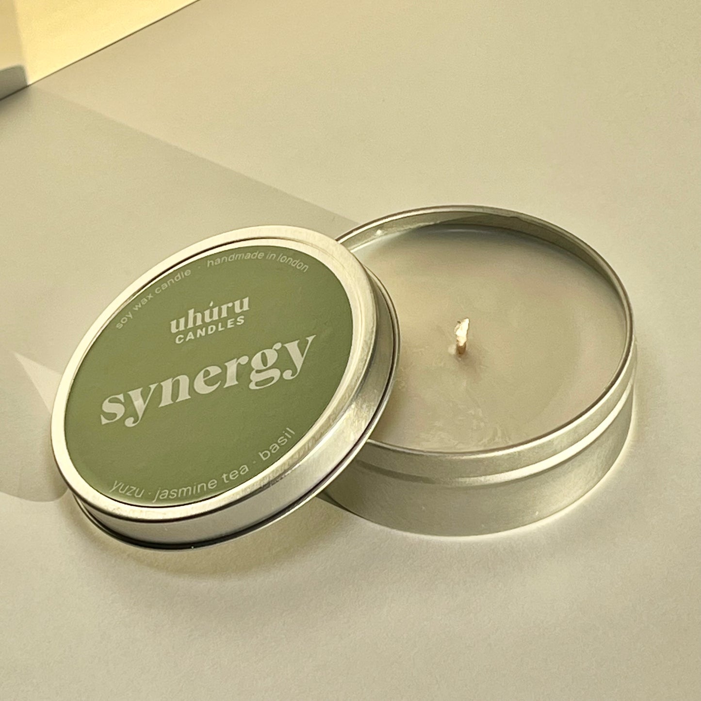 Synergy by Uhuru Candles - yuzu, jasmine tea and basil scented soy wax candle in metal tin container with lid off. Tin net weight 70g.